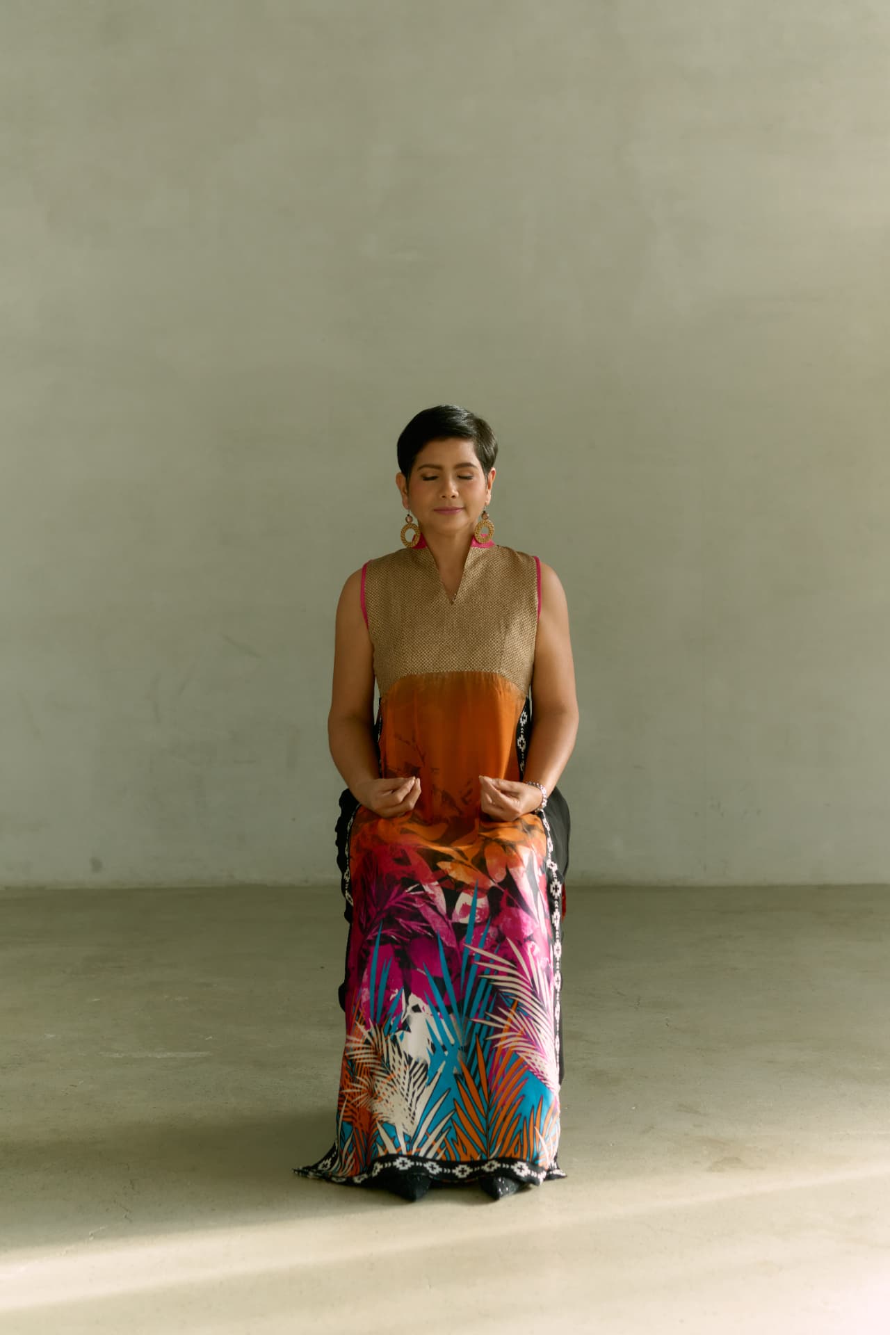 Angelica Umali seated in stillness with eyes closed, wearing a vivid tropical print gown